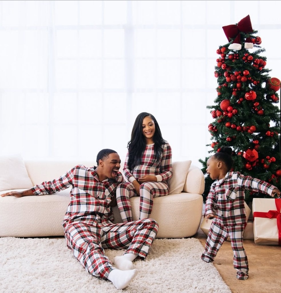A joyful family in matching plaid pajamas sits by a decorated Christmas tree. They are on a white couch, exuding warmth and happiness.