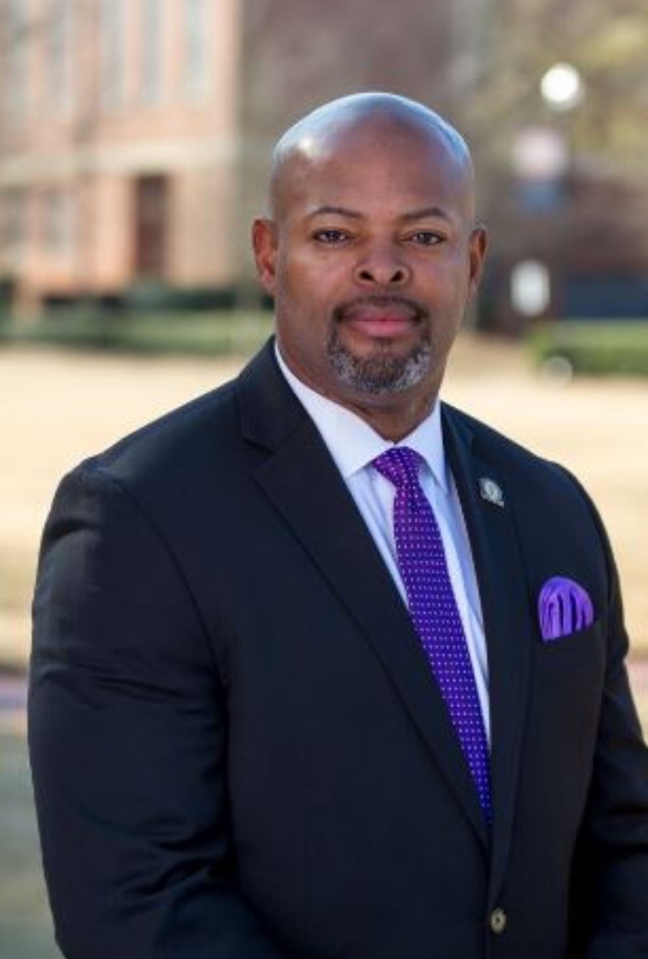 Portrait of a man in a dark suit with a purple tie and pocket square